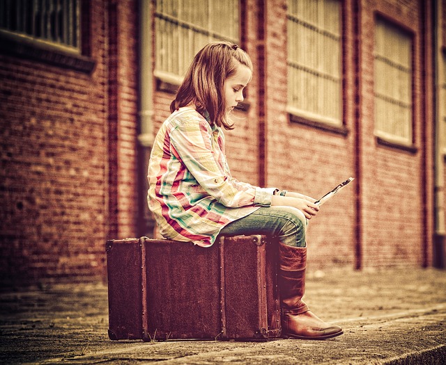 Kind sitzt auf Koffer und liest