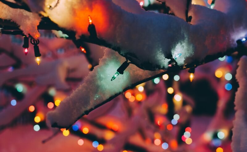 Bunte Lichterkette an Weihnachtsbaum mit Schnee
