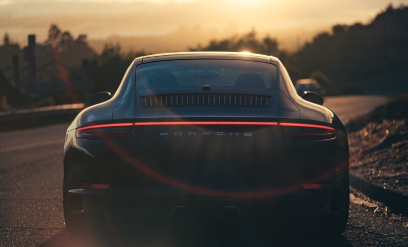 Schwarzer Porsche Sportwagen von hinten mit Sonnenuntergang