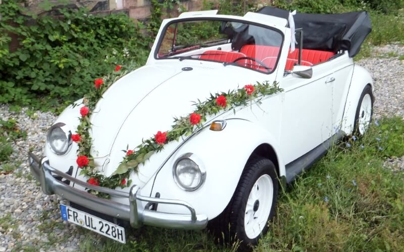 Weißer VW Käfer Cabrio mit Blumenschmuck als Hochzeitsfahrzeug