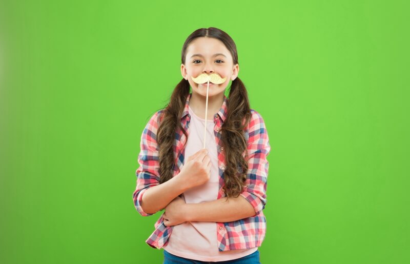 Mädchen posiert mit Schnurrbart am Stil vor Greenscreen