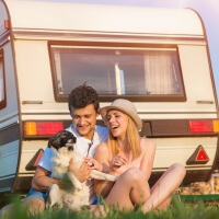 Junges Paar mit Hund vor Wohnwagen im Gras