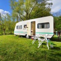 Wohnwagen auf grüner Wiese mit Gartenmöbeln